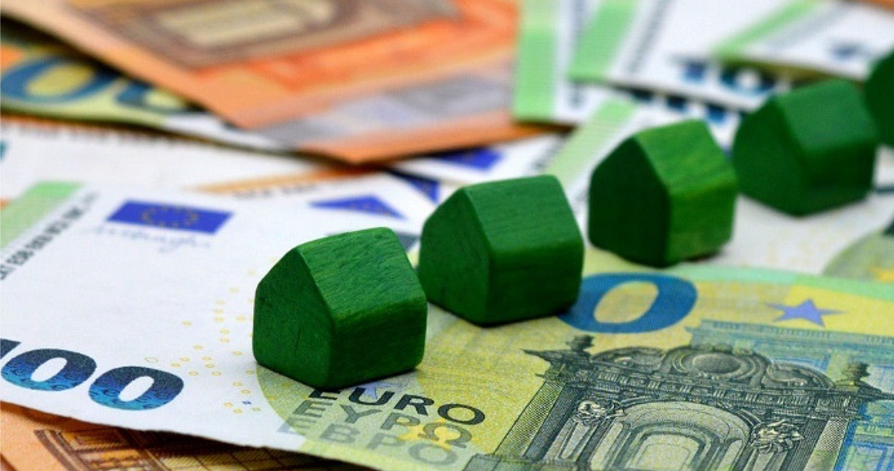 Bausparen Banner Mehrere grüne Miniaturhäuschen liegen auf verschiedenen Euro-Geldscheinen.