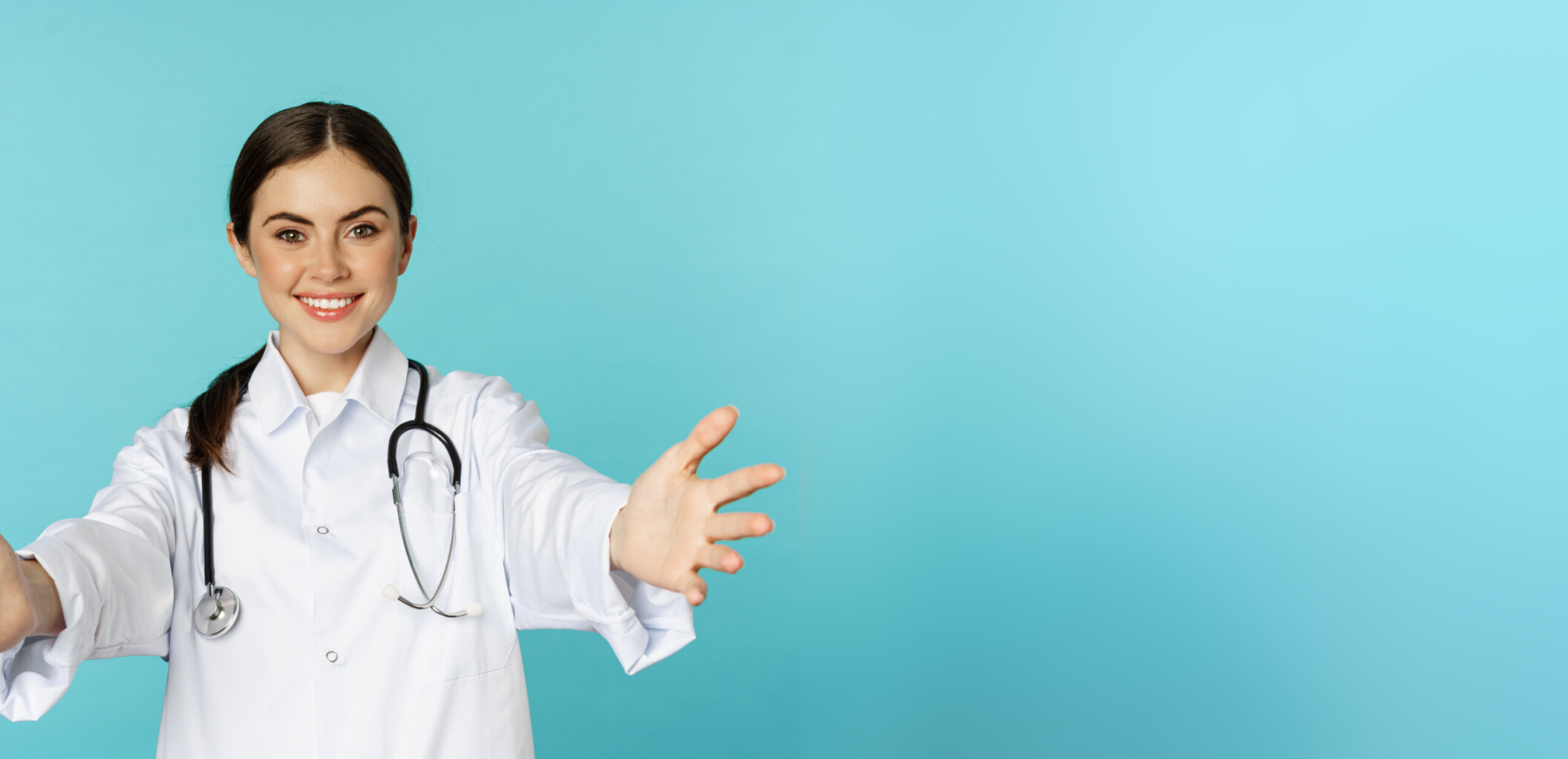 Smiling friendly doctor, girl healthcare worker, intern reaching hands, inviting, hugging or receiving in arms, standing over torquoise background